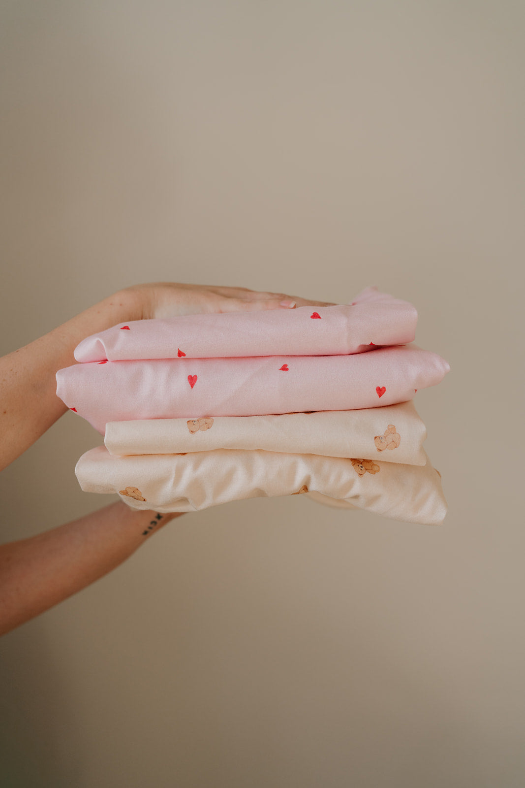 Hands holding a folded stack of Darling Heart and Tiny Teddy waterproof fitted sheets
